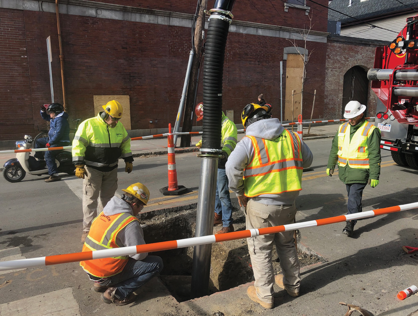 A crew uses an air excavation machine to work on a busy road.
