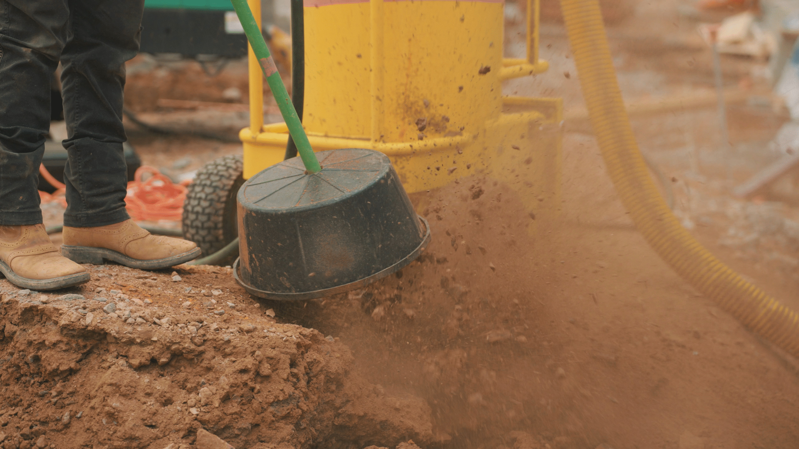 Close-up of worker using air spade tool with a black splash guard to break up red soil.